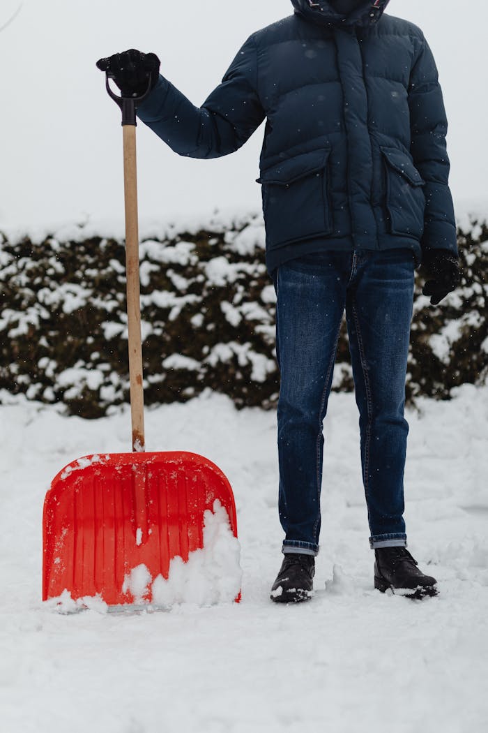 Services Person in winter clothing shoveling snow outdoors with bright red shovel.